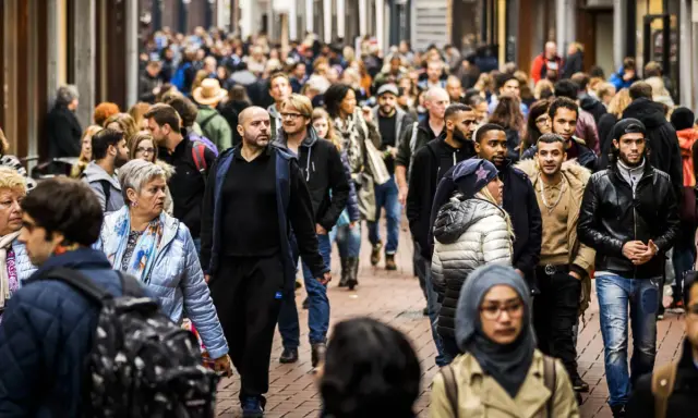A diverse crowd of people walks down a busy street in the Netherlands.