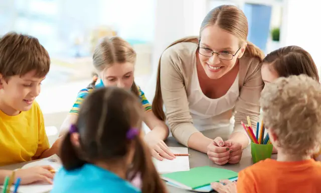 Docente begeleidt kinderen bij creatieve check-in werkvormen onderwijs. Kleurrijke potloden en notitieboekjes op tafel.