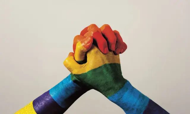 Twee handen, beschilderd met de regenboogkleuren, omstrengeld. Een symbool van verbondenheid en de strijd voor sociale rechtvaardigheid.