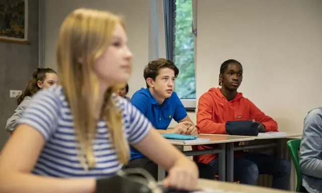 Leerlingen in een klaslokaal, met een jongen in een blauw shirt die aandachtig luistert. Dit beeld toont leuke manieren om je klas stil te krijgen.