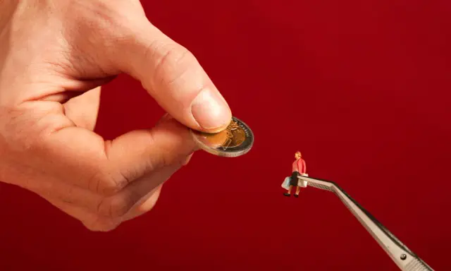 Een hand houdt een munt vast, terwijl een pincet een miniatuurfiguur met boodschappentassen vasthoudt. Dit symboliseert hoe een filantroop helpt.