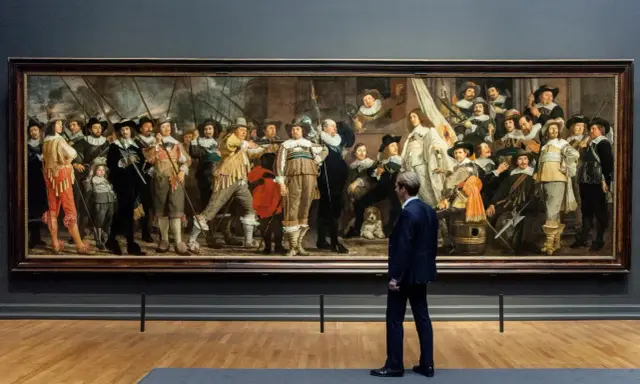 Man kijkt naar De Nachtwacht, een schilderij dat de Nederlandse nationale identiteit weerspiegelt met zijn dynamische groepsportret van schutters.