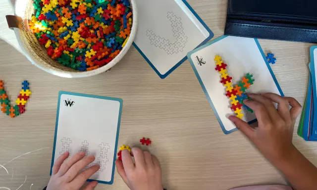 Kinderen bouwen met kleurrijke stukjes aan patronen op kaarten. Een mand vol bouwstenen ligt klaar voor meer taal spelletjes.