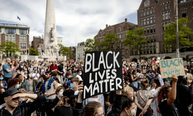 Mensen demonstreren op een plein met een monument, sommigen dragen borden met "Black Lives Matter".
