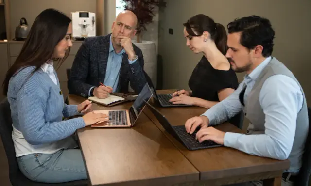 Teamoverleg: de betekenis van delegeren wordt duidelijk als de manager taken verdeelt en de teamleden geconcentreerd werken aan hun laptops.