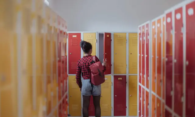 Meisje met rugzak bij schoolkluisjes. Ze overweegt of ze van 3 havo naar 4 mavo kan.