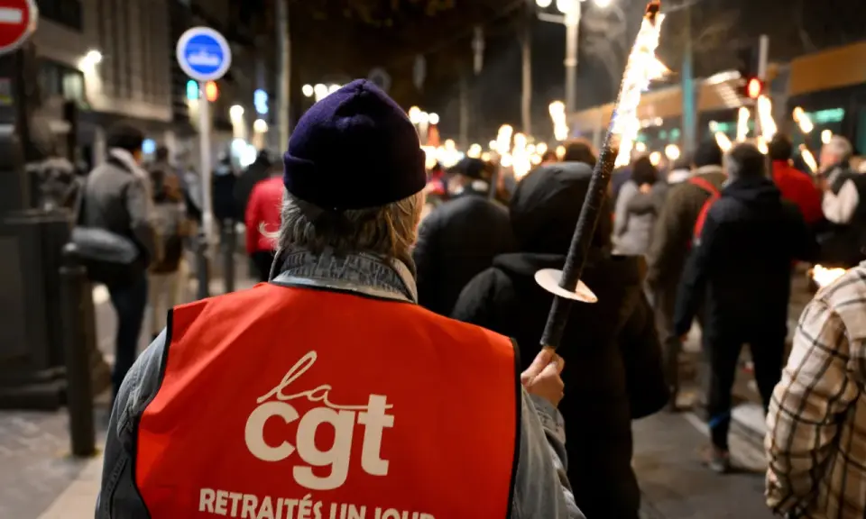 Demonstranten met fakkels protesteren tegen de pensioenleeftijd in Frankrijk. Op de rode vesten staat "CGT".