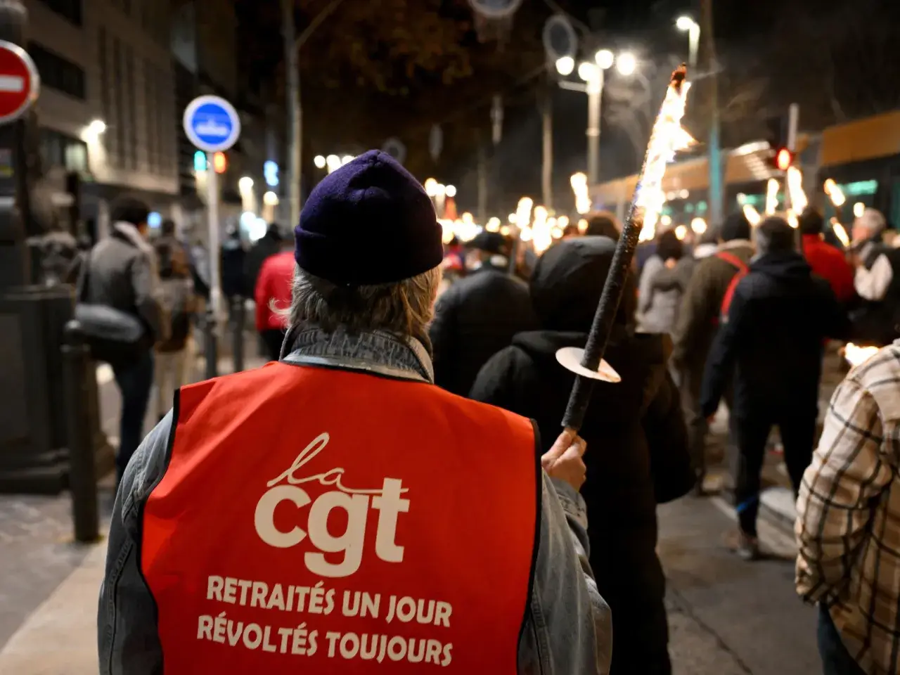 Demonstranten met fakkels protesteren tegen de pensioenleeftijd in Frankrijk. Op de rode vesten staat "CGT".