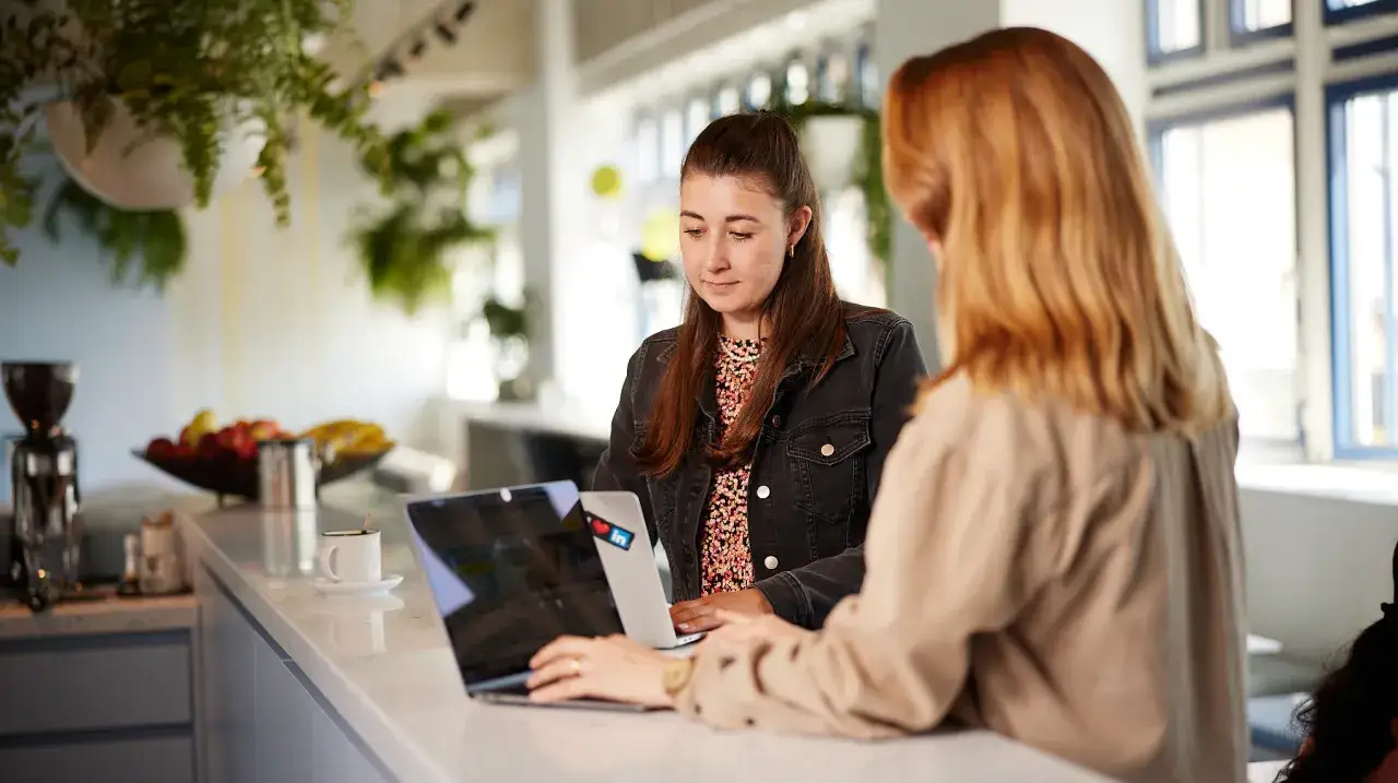 Twee vrouwen werken aan laptops. Een stagiaire krijgt feedback, een voorbeeld van een leerzame werkplek.