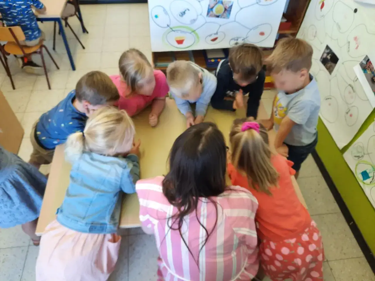 Kinderen leren spelenderwijs met de karakter methode. Ze staan rond een tafel, geconcentreerd op een tekening.