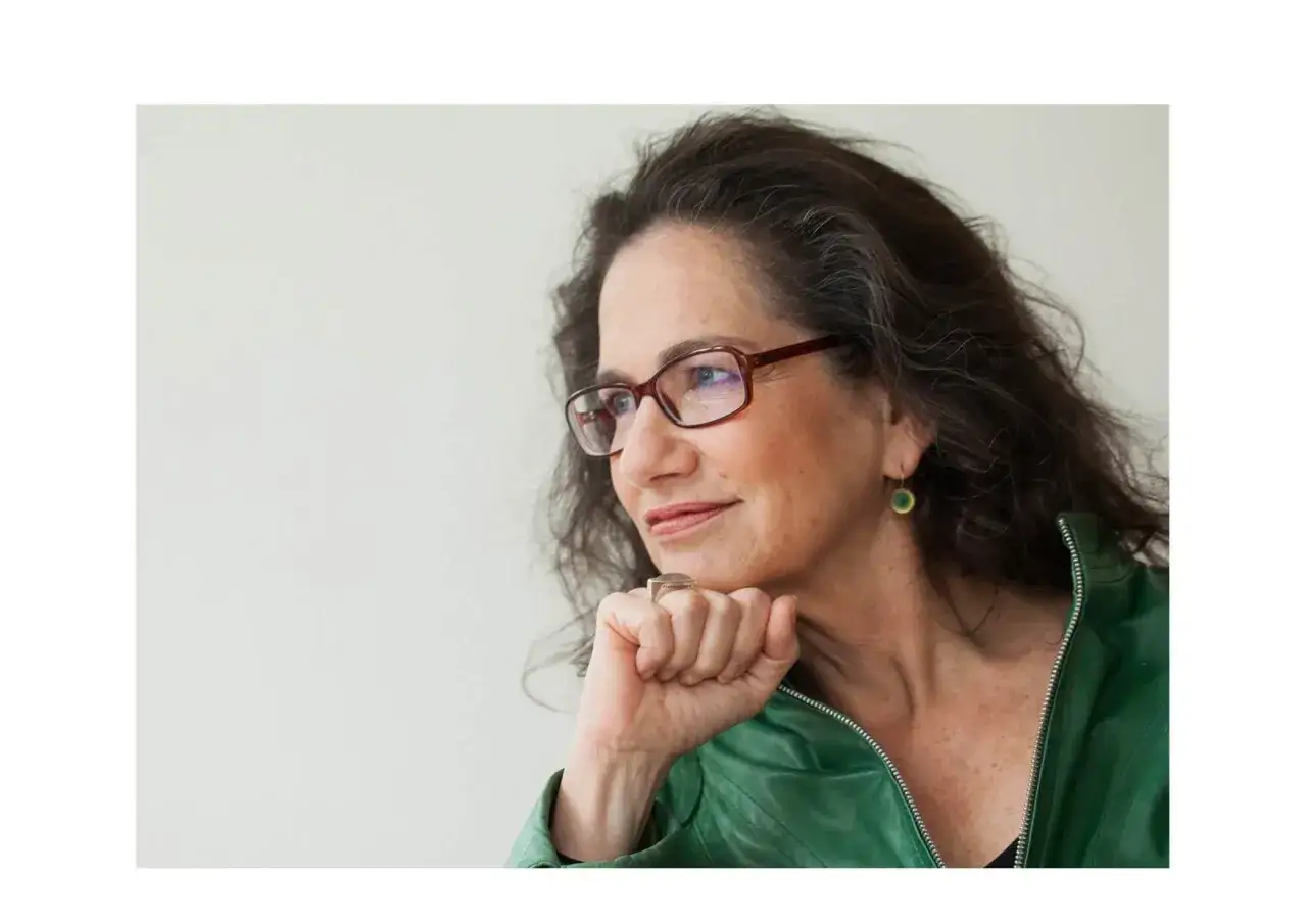 Susan Neiman, met bril en groene jas, denkt na met haar kin op haar vuist.