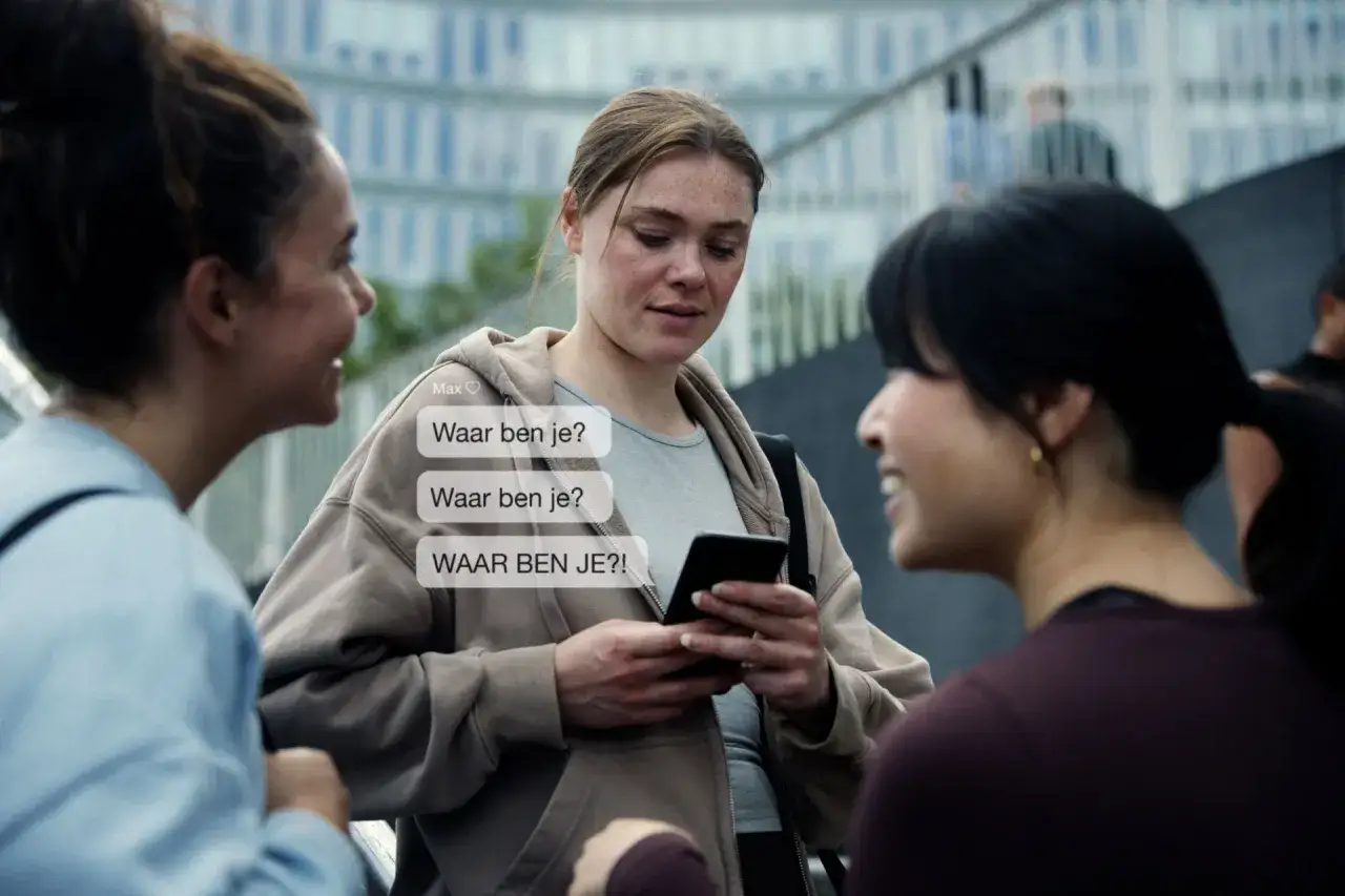 Drie vrouwen praten, &eacute;&eacute;n kijkt bezorgd naar haar telefoon met berichten als 