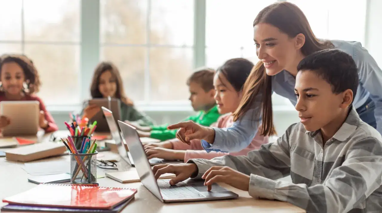 Docente helpt leerlingen met laptops en tablets. Mooie voorbeelden van blended learning in de klas.