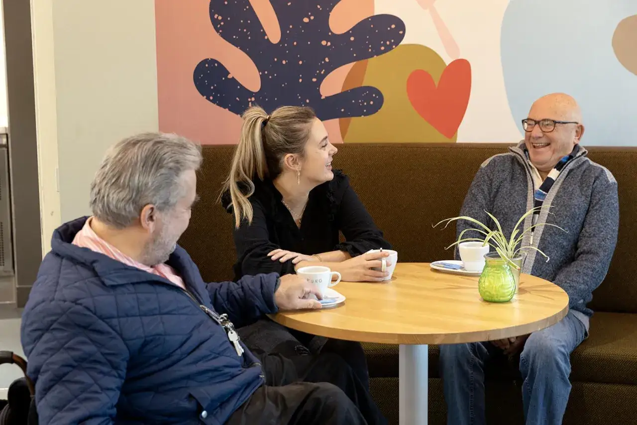 Drie mensen genieten van een kopje koffie en een goed gesprek, wat de sociale cohesie versterkt.