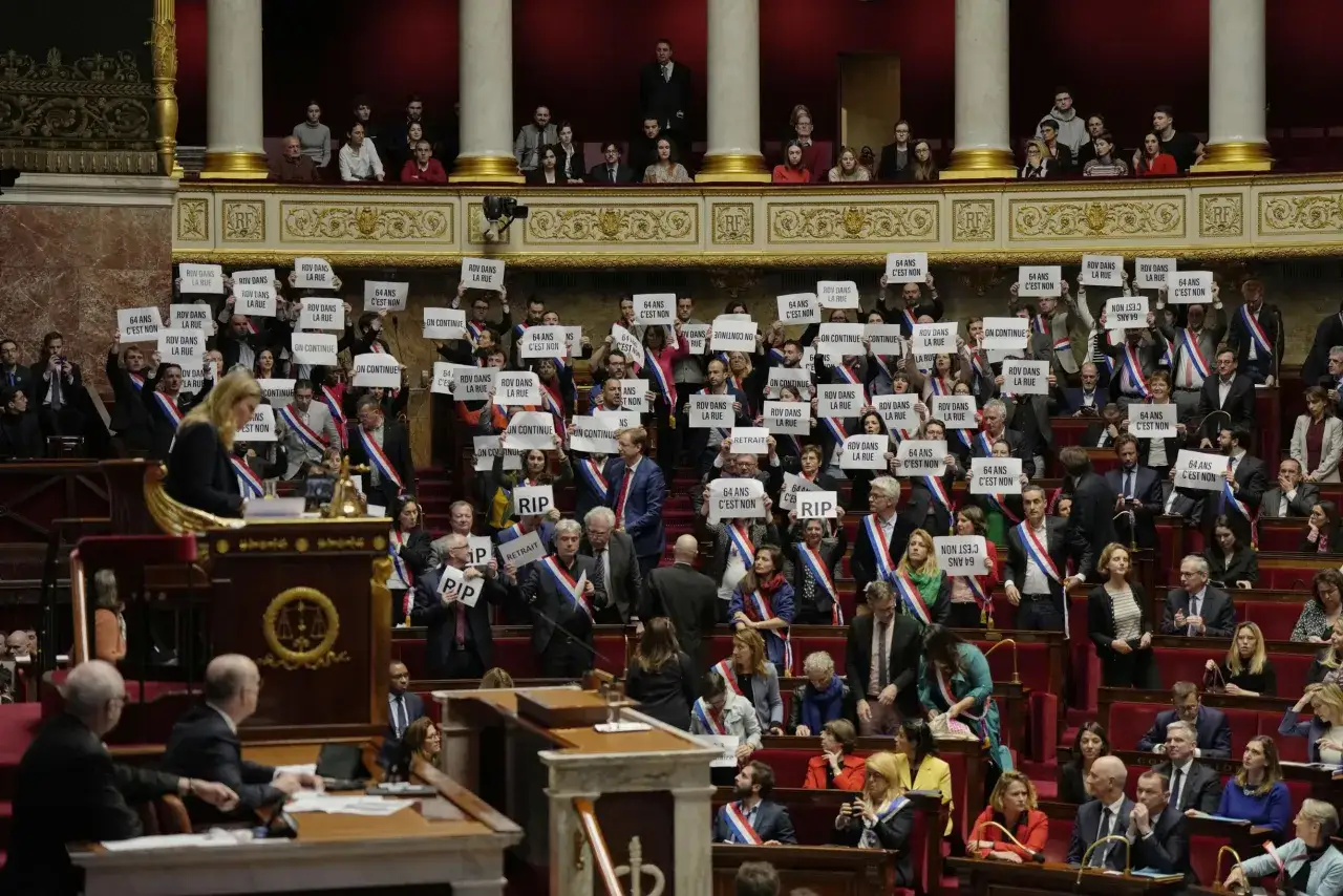 Protest in het Franse parlement tegen de verhoging van de pensioenleeftijd. Mensen houden borden omhoog met
