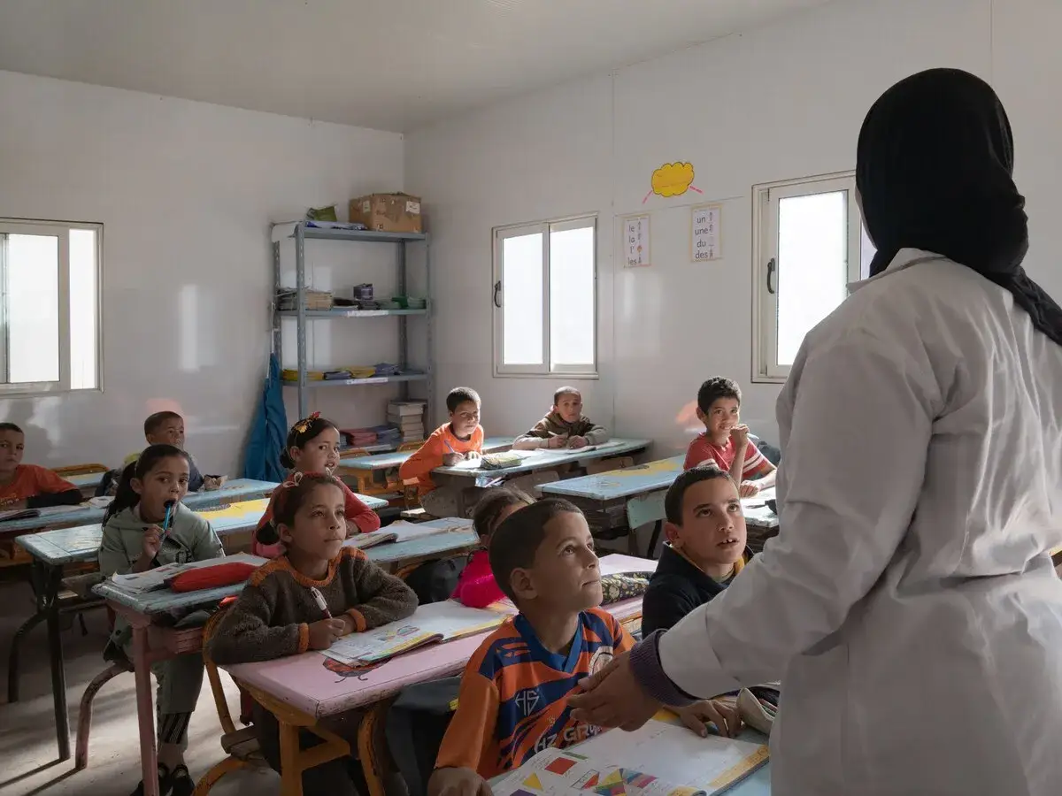 Klaslokaal met kinderen, waaronder Marokkaanse Nederlanders, die luisteren naar hun lerares.