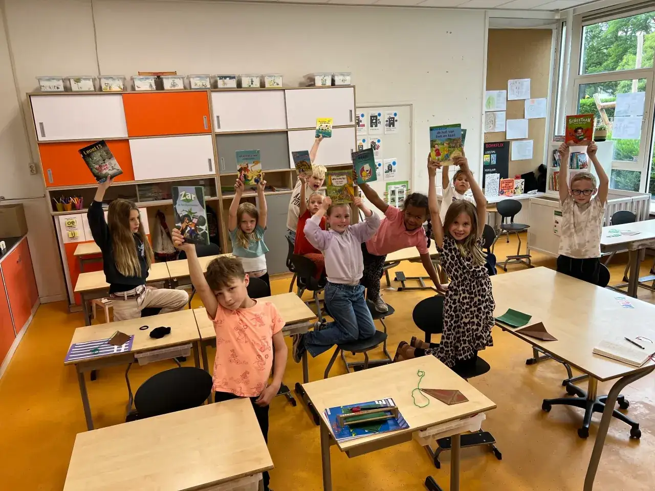 Kinderen uit groep 4 houden boeken omhoog tijdens een boekbespreking. Ze zijn enthousiast en delen hun favoriete verhalen.