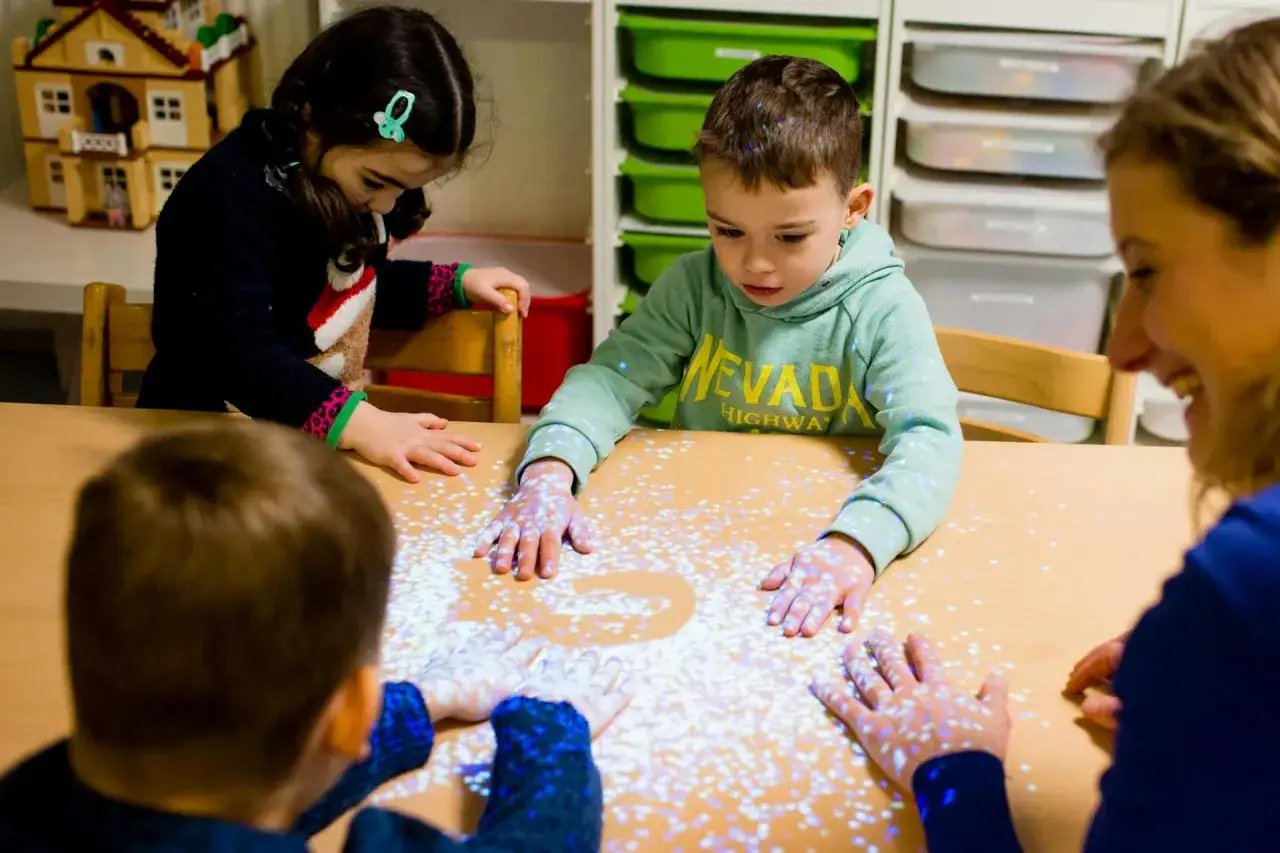 Kinderen en een volwassene spelen met interactieve taal spelletjes op een tafel, met lichtprojecties op hun handen.