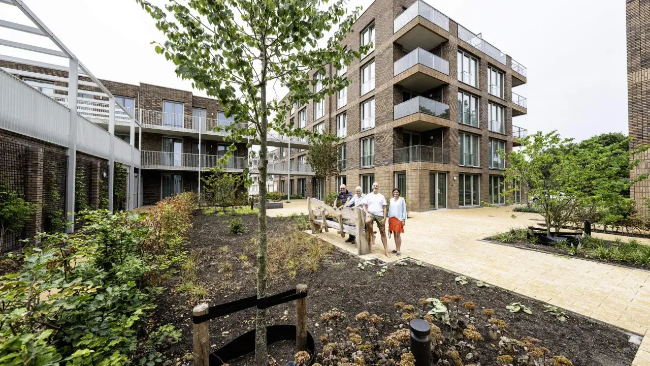 Vier mensen genieten van de zon op een bankje in de tuin van een modern appartementencomplex. Ze lijken te vieren dat ze volwassen worden.