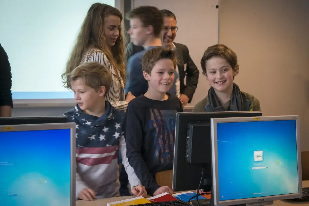 Kinderen leren met verschillende werkvormen op computers. Een lerares en een leraar kijken toe.