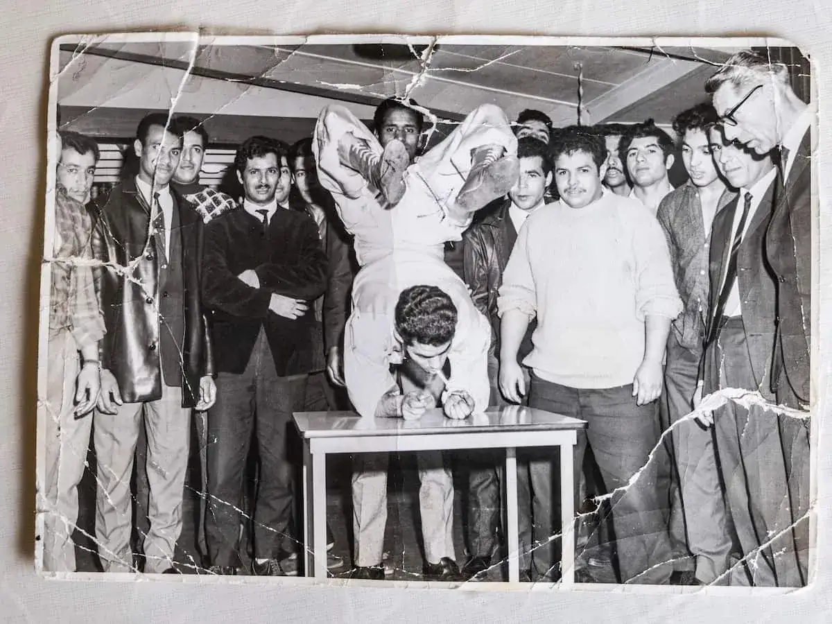 Jongemannen uit Marokko NL verhalen. Een acrobatische pose op een tafel, omringd door toeschouwers.