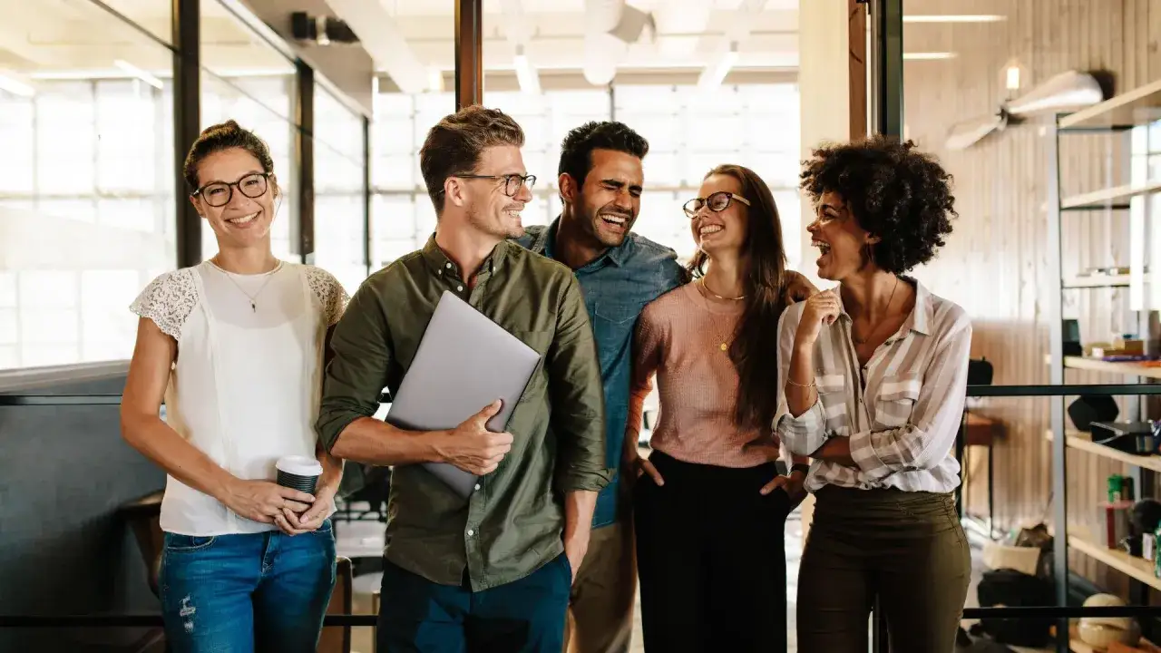 Een diverse groep collega's lacht en praat, wat een sfeer van een inclusieve werkomgeving uitstraalt.