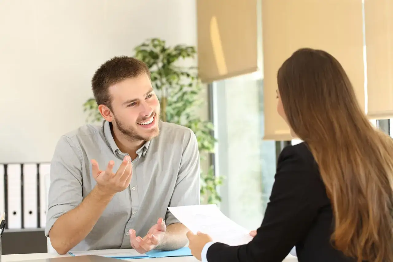 Man en vrouw voeren een beoordelingsgesprek. De man legt iets uit met zijn handen, de vrouw houdt een document vast.