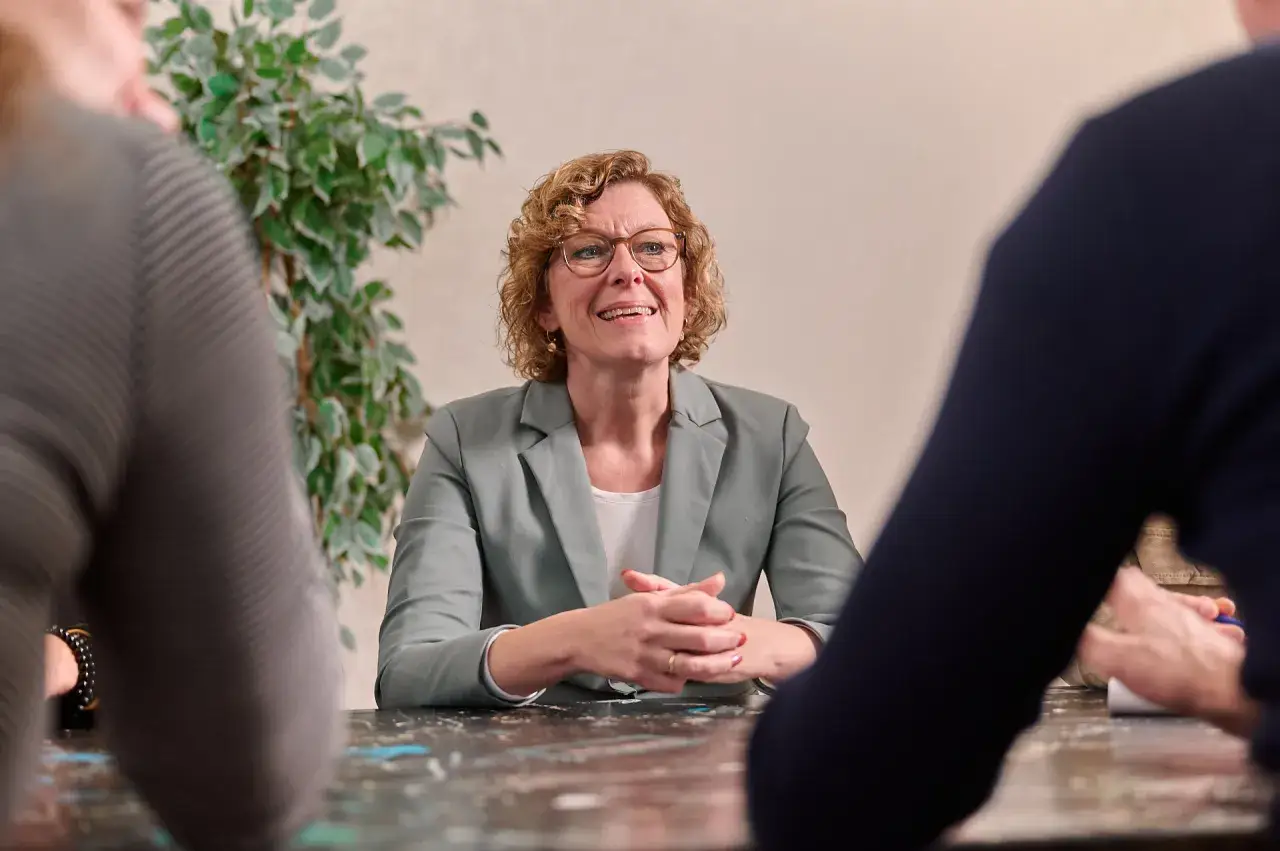 Een vrouw met een bril en krullend haar bespreekt duurzame inzetbaarheid met collega's aan een tafel.
