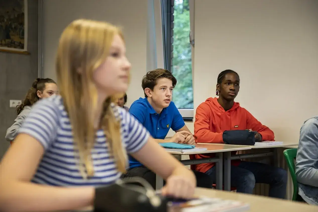Leerlingen in een klaslokaal, een jongen in blauw en een jongen in oranje, luisteren aandachtig. Leuke manieren om je klas stil te krijgen beginnen met aandacht.