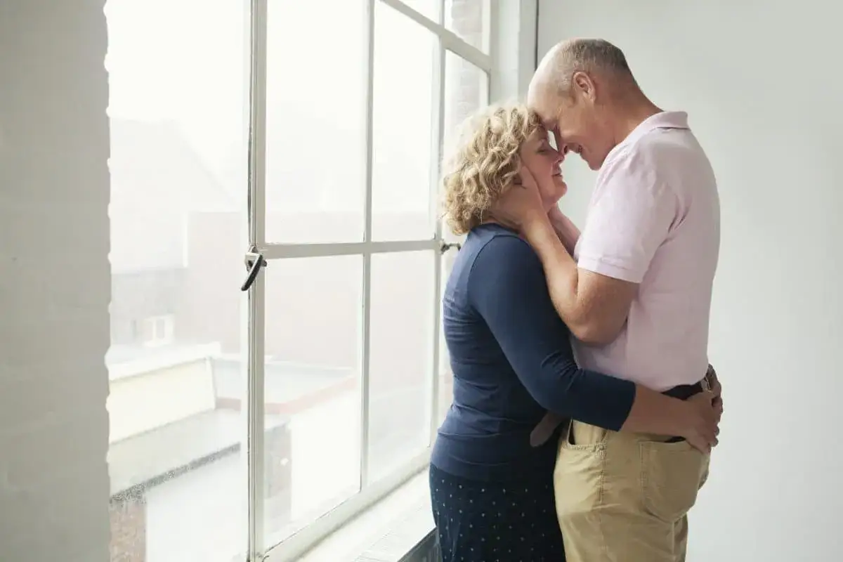 Een stel omhelst elkaar bij een raam. Ze hebben gekozen voor een leven als bewust kinderloos, vol liefde voor elkaar.