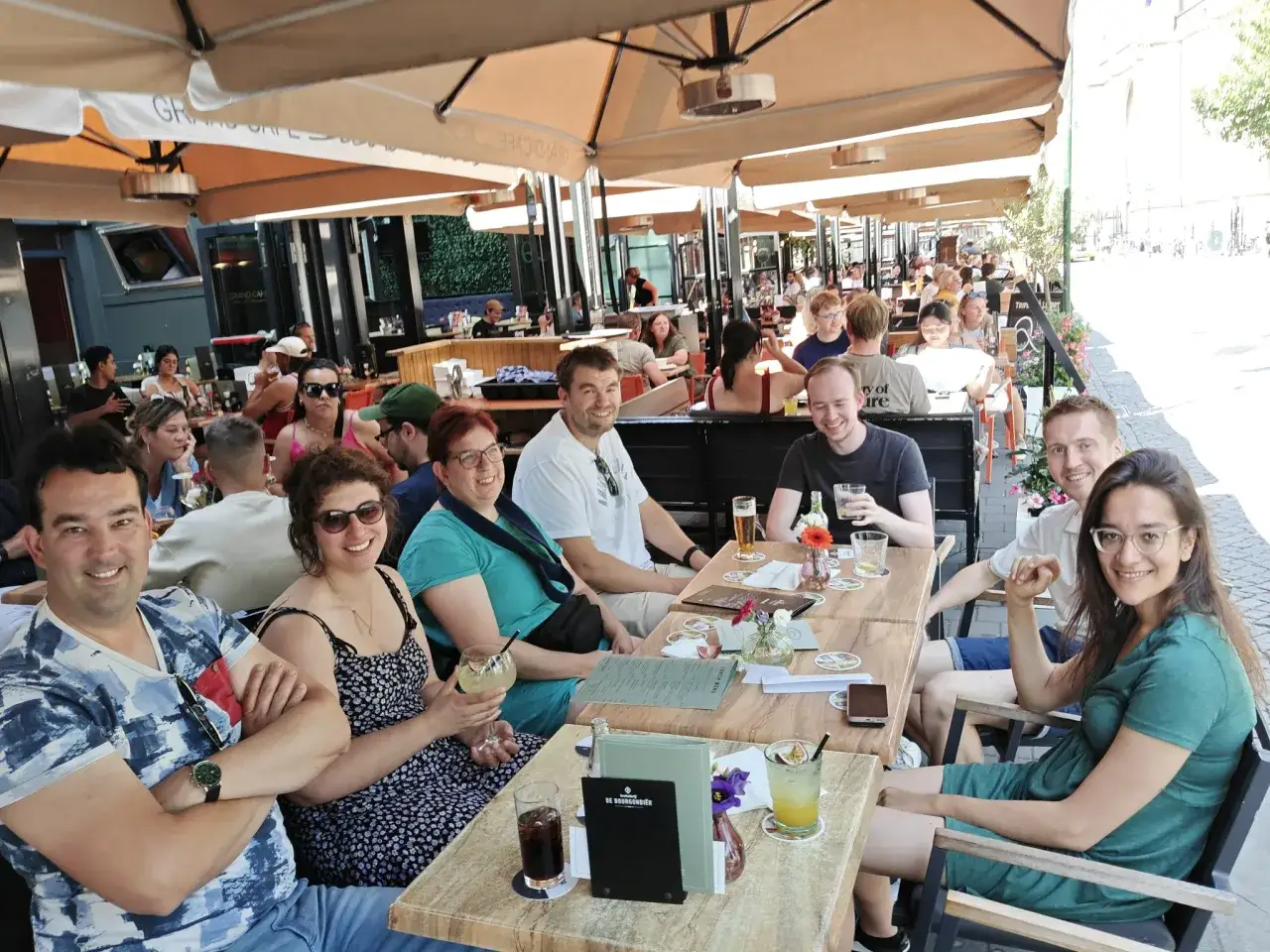 Groep vrienden geniet van een zonnige dag met drankjes en goed gezelschap, wat de waarde van sociale contacten benadrukt.